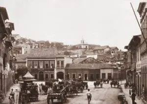 Uma praça urbana antiga em preto e branco, com carruagem e edifícios.