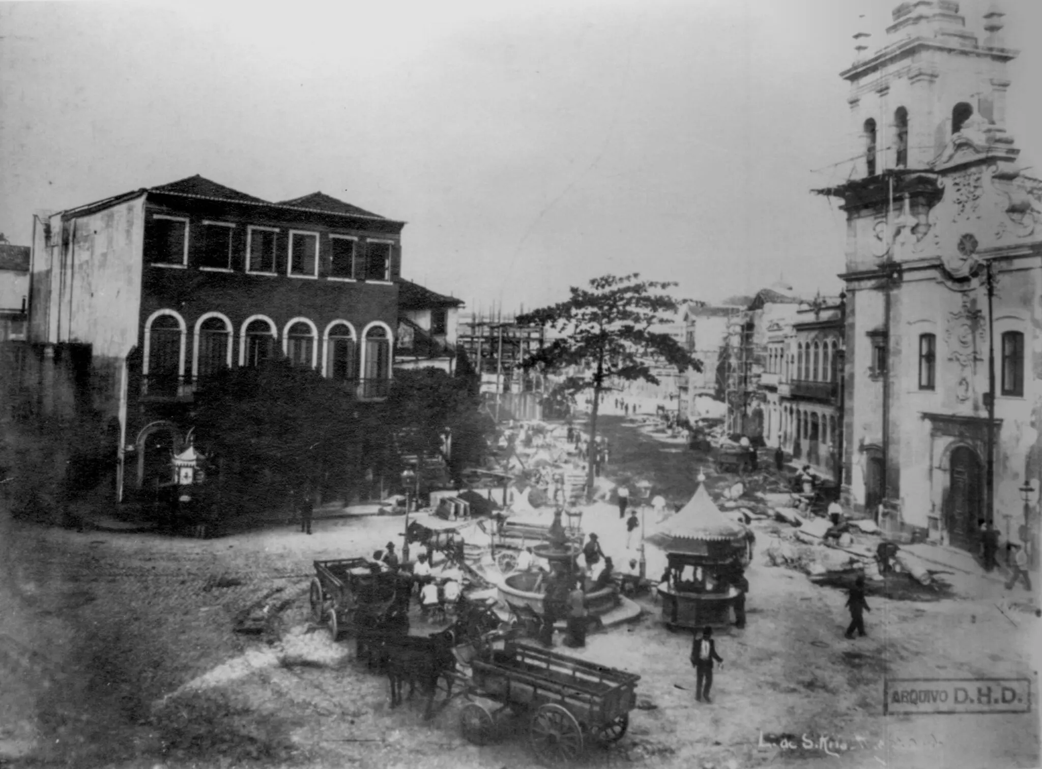 Uma praça histórica com fonte e igreja.