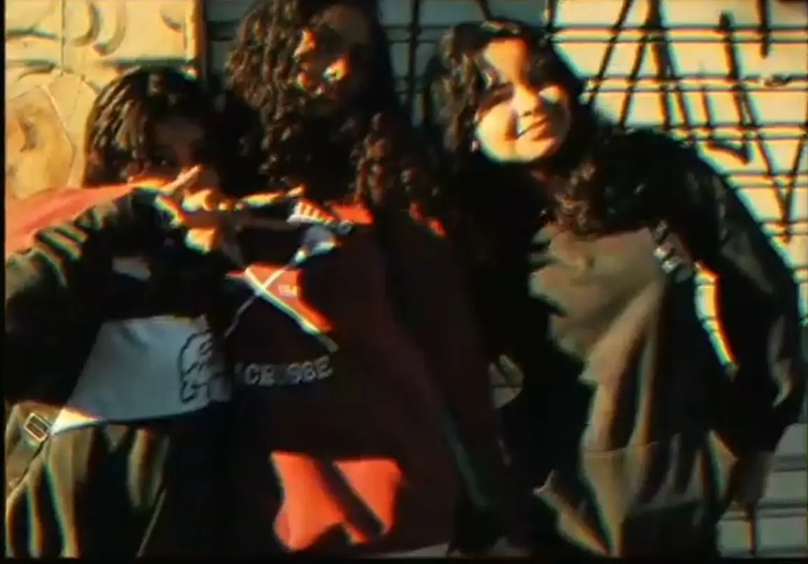 Três pessoas sorridentes em tons vintage, com grafite e grade ao fundo.