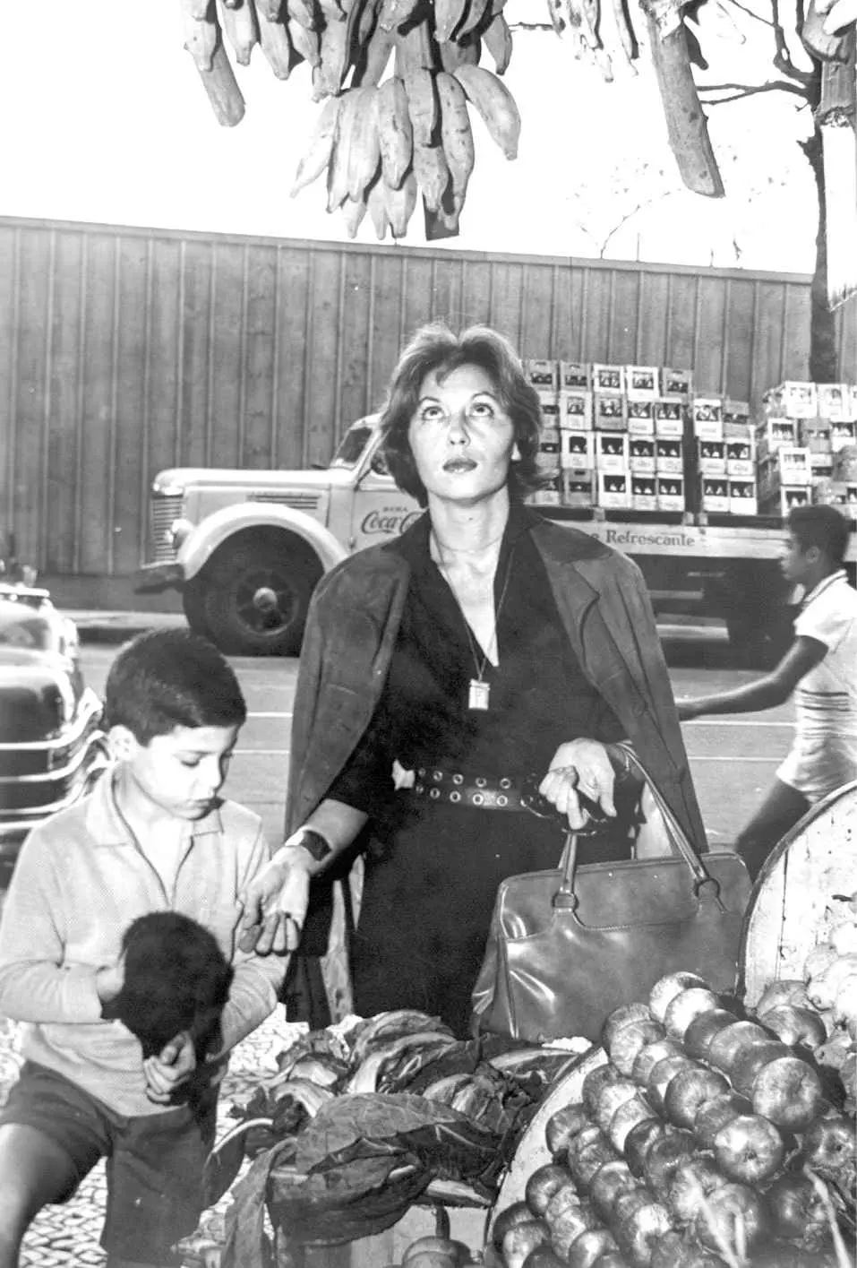 Mulher e dois meninos em mercado com bananas pendentes.