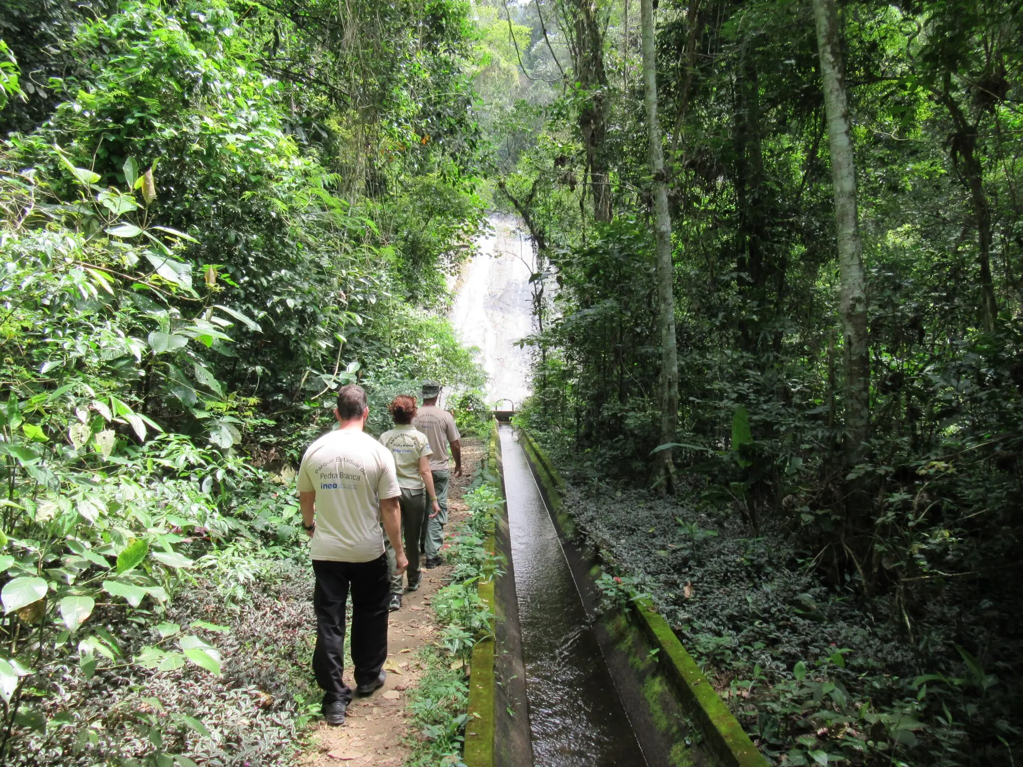 Parque natural com pessoas caminhando e cachoeira ao fundo.