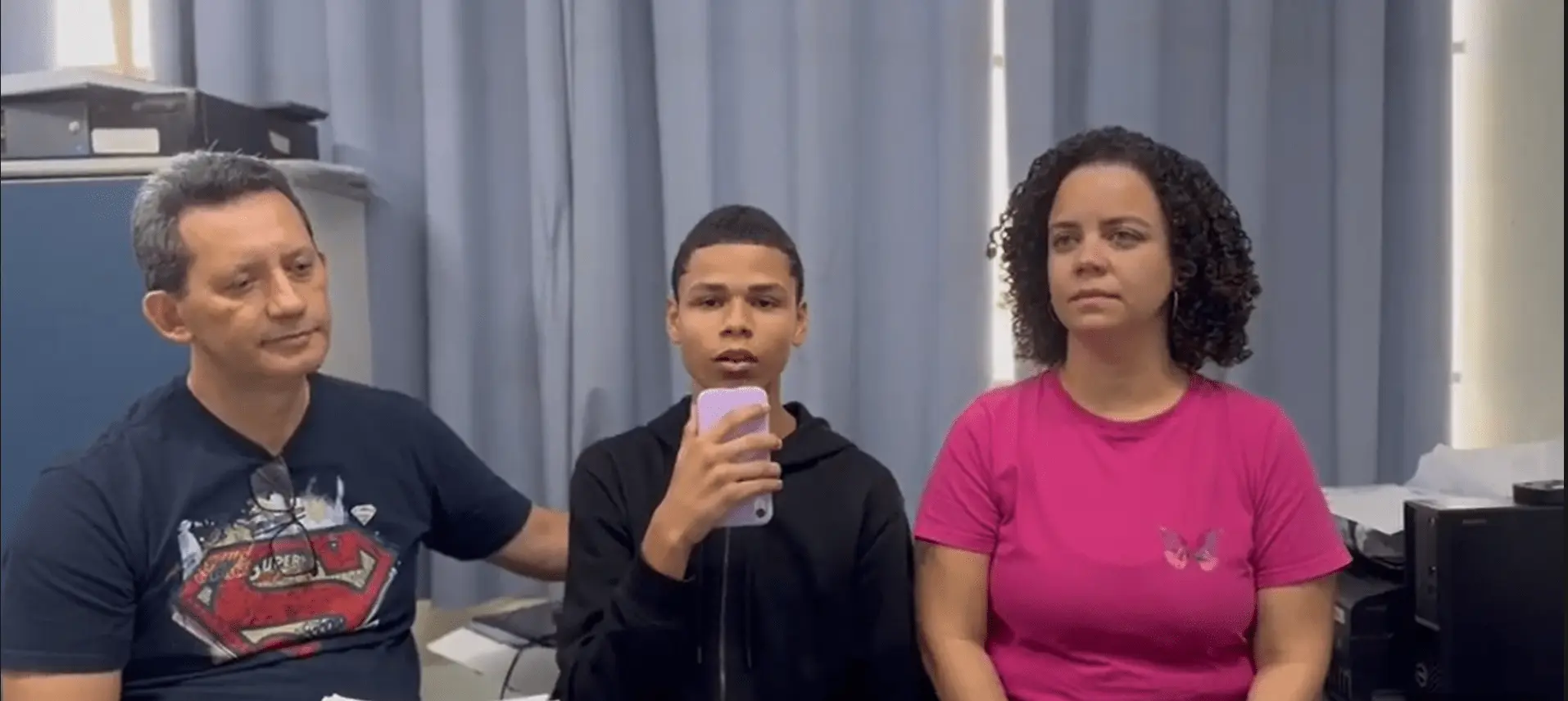 Três pessoas sentadas lado a lado em uma sala de espera médica.