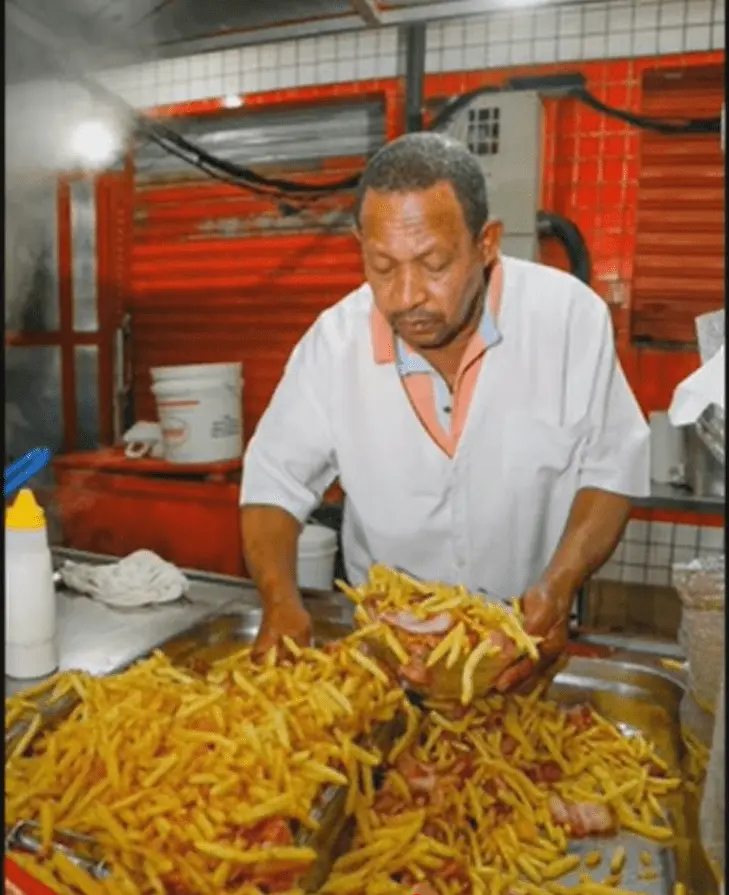 Homem cozinhando batatas fritas e carne em cozinha industrial.
