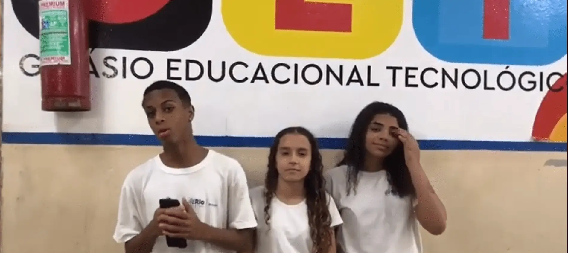 Três crianças em frente a um painel educacional tecnológico.