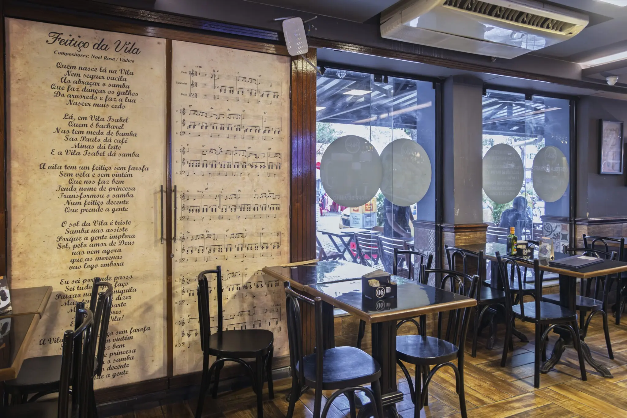 Sala de restaurante com decoração musical e pessoas caminhando pela rua ao fundo.