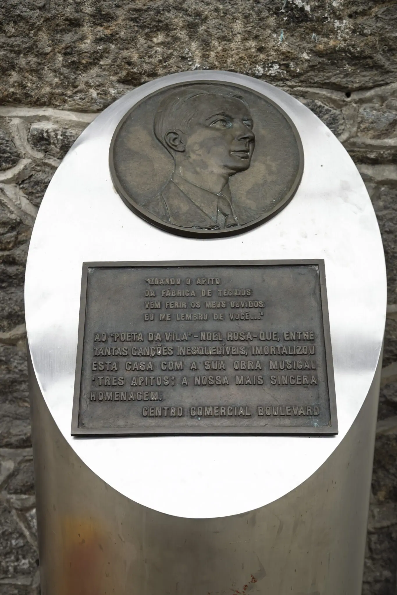 Monumento comemorativo com placa circular e relevo em bronze.
