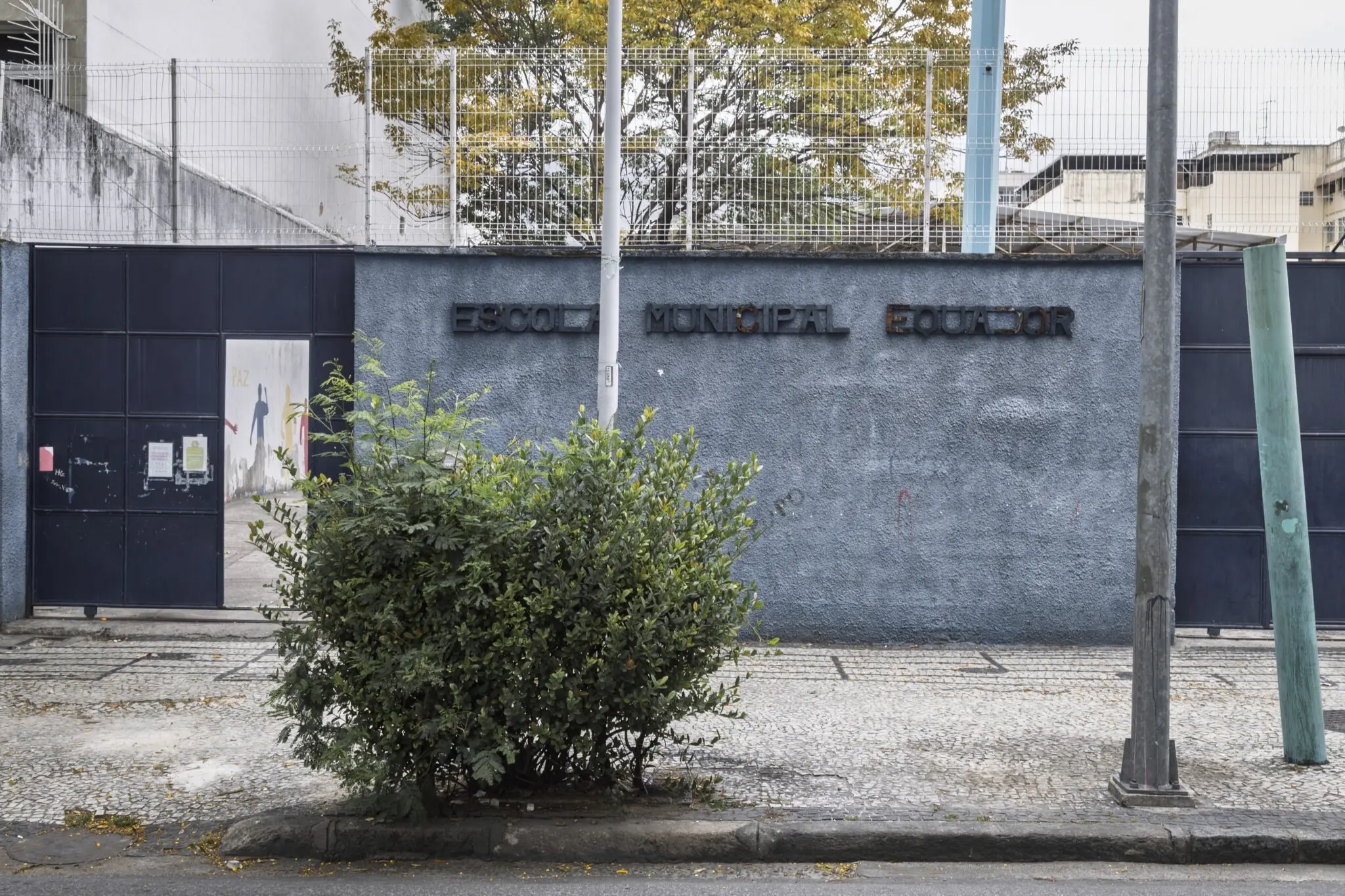 Fachada cinza da Escola Municipal Equador com porta fechada e árvore verde.