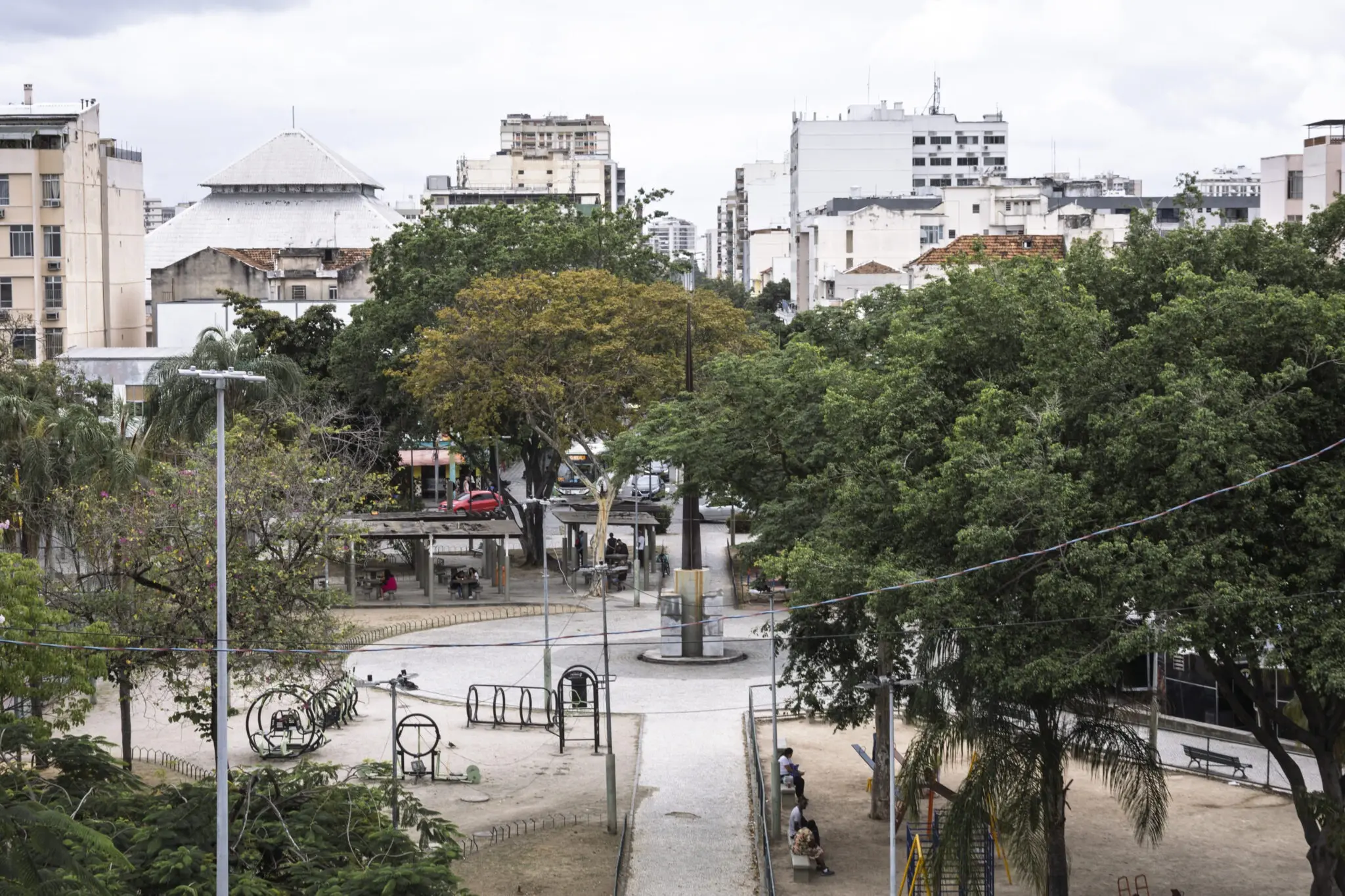 Praça urbana com árvores, bancos e edifícios residenciais.