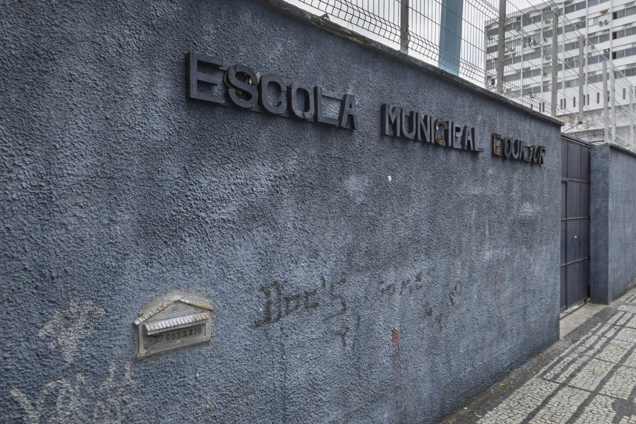 Parede de escola municipal com inscrição e grade metálica.