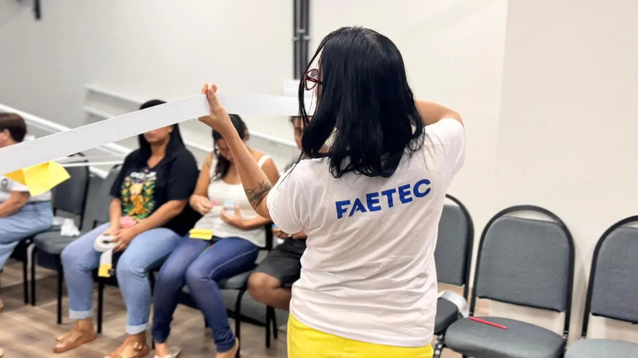 Sala de conferências com mulher segurando papel e pessoas conversando ao fundo.