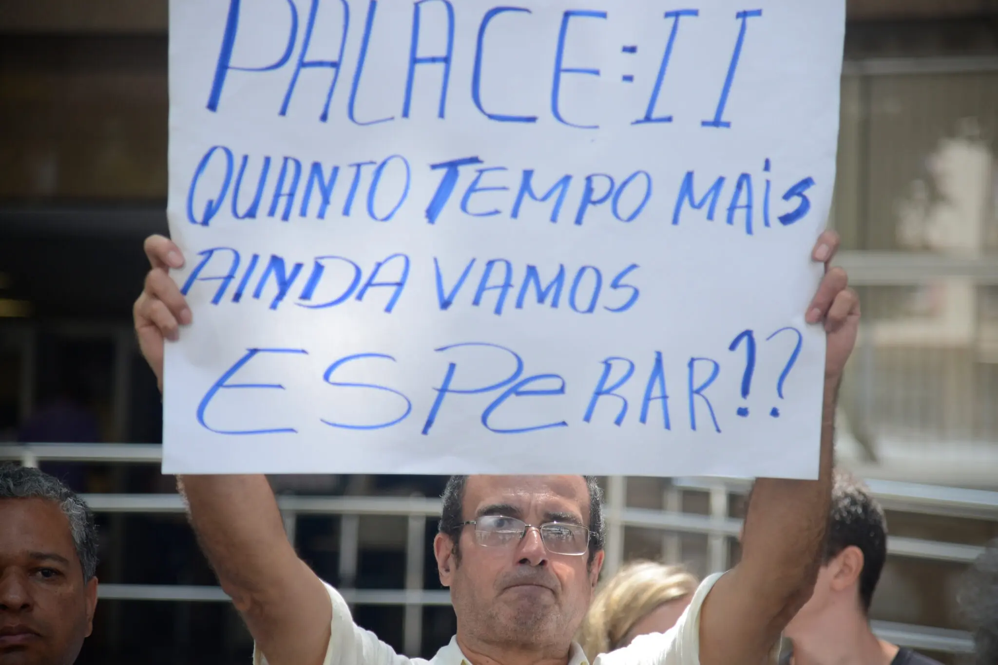 Protesto em frente ao TJ-RJ; homem segura cartaz pedindo fim da espera.