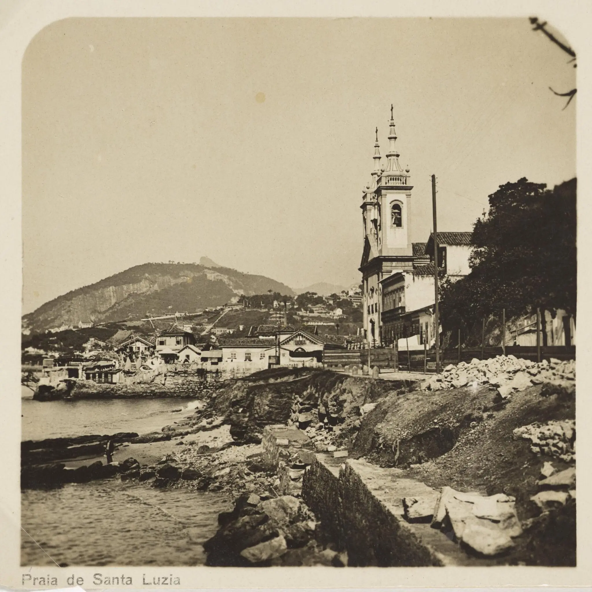Praia antiga com casas, igreja e colina.