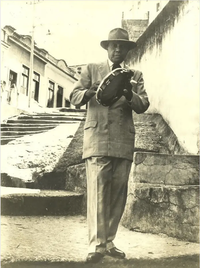 Homem em terno clássico e chapéu em rua preto e branco.