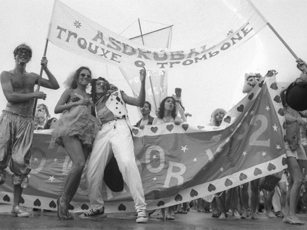 Fotografia preto e branco de uma procissão festiva com dança e bandeiras.