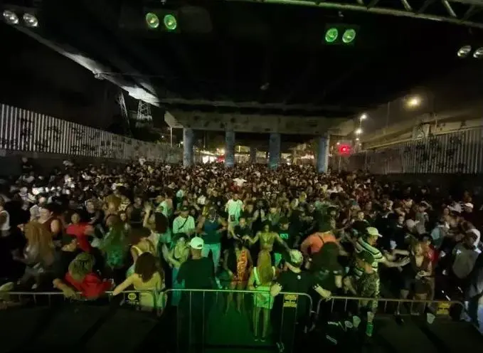 Multidão dançando ou assistindo a performance em viaduto iluminado.