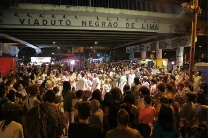 Multidão caminhando sob viaduto à noite, sinal "Viaduto Negro de Lima".