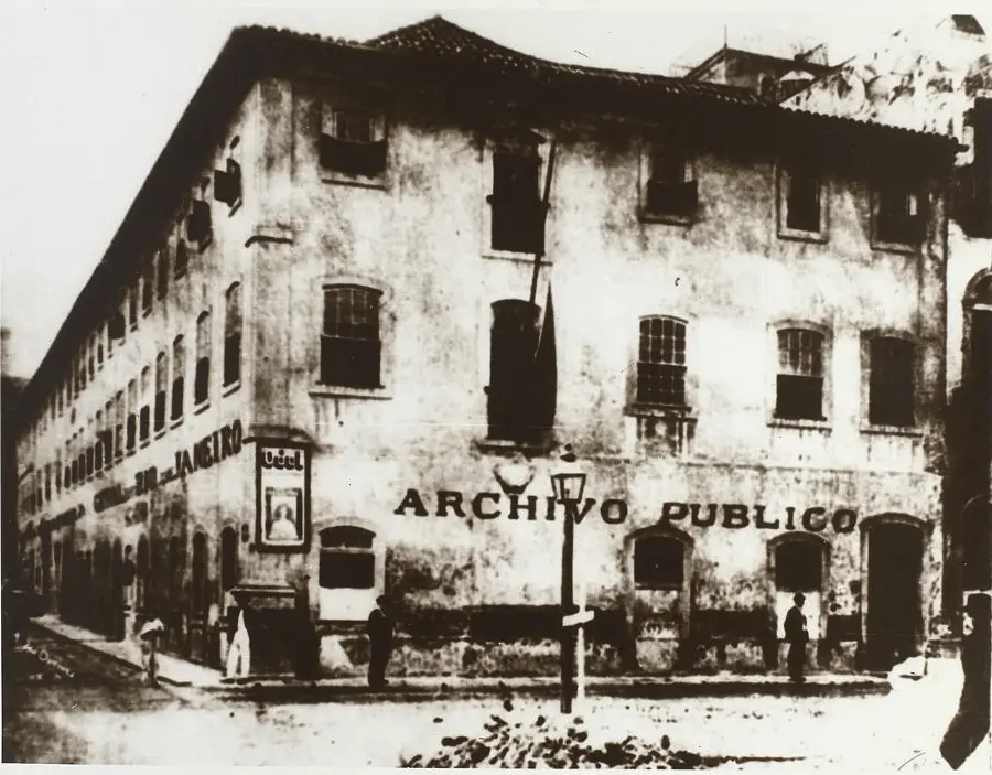 Edifício antigo com "ARCHIVO PUBLICO" na fachada, arcos e janelas menores à esquerda, placa "JANERO" ao centro, grandes janelas retangulares à direita.