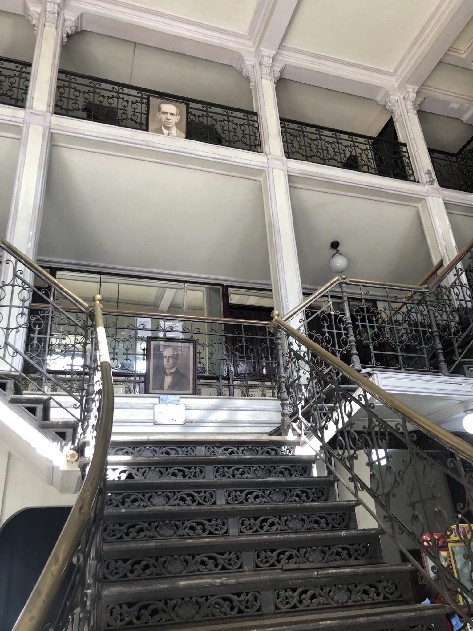 Escadaria com elementos decorativos em ferro forjado, retrato de homem em terno pendurado.