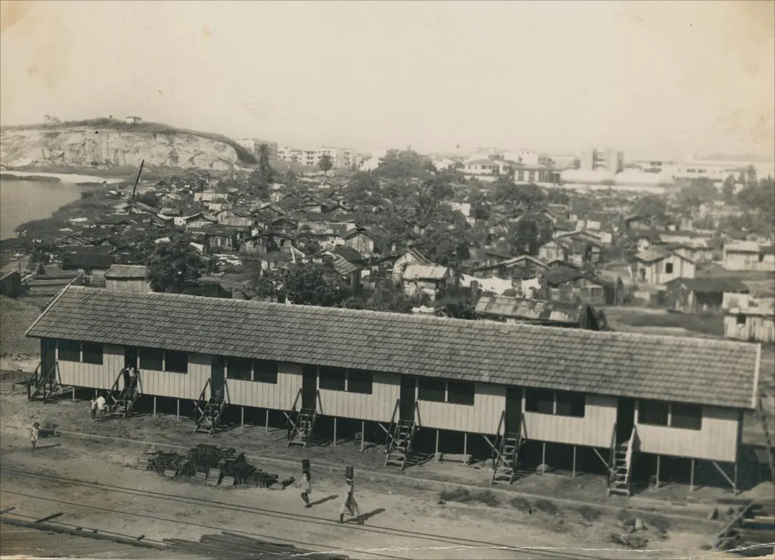 Fotografia preto e branco de favela com edifícios baixos e áreas urbanas ao fundo.