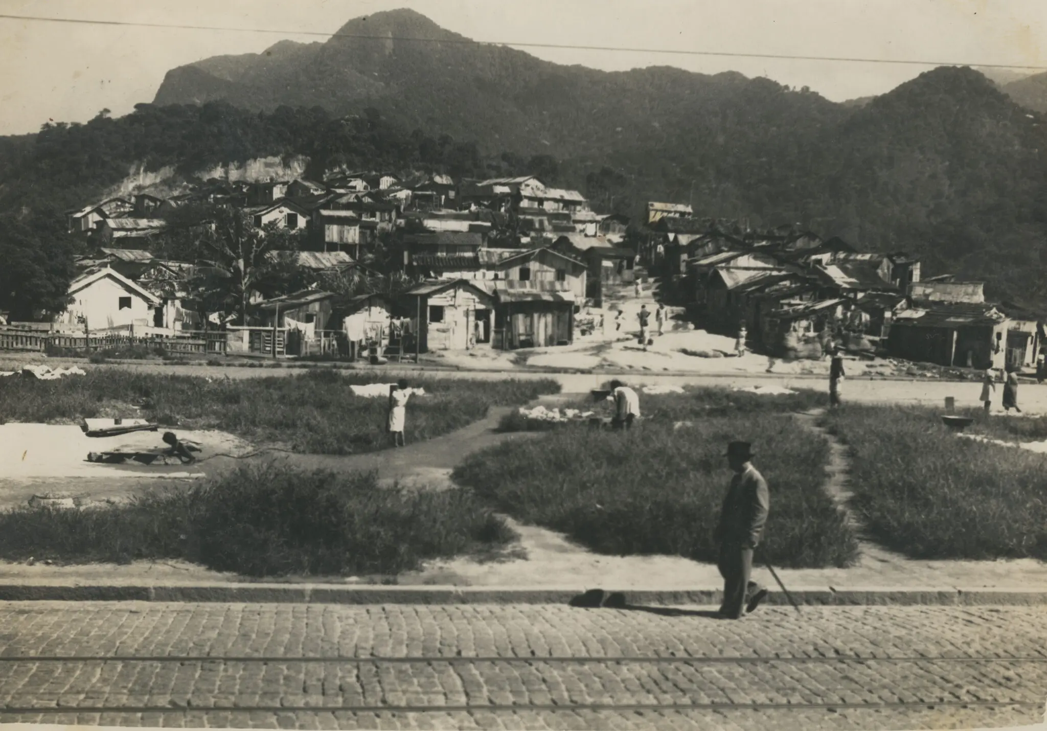 Fotografia preto e branco de favela com casinhas de madeira e montanha verde.