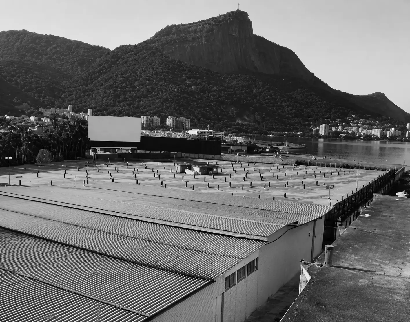 Drive-in em preto e branco com estrutura, montanha, edifícios e telhado industrial.