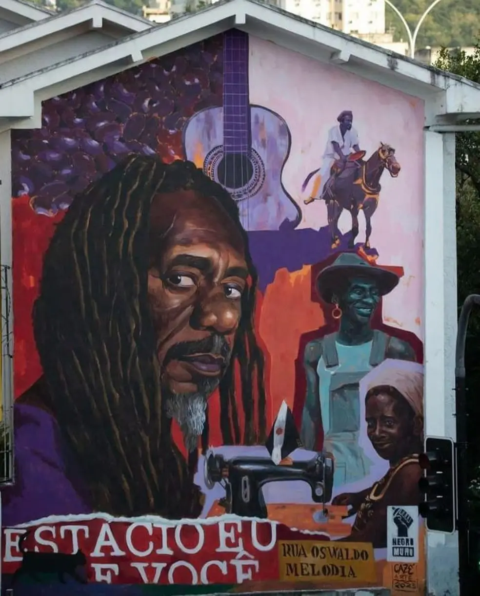 Pintura mural colorida com rosto de homem, guitarra, cavalo, mulher sorridente com máquina de costura e criança olhando.