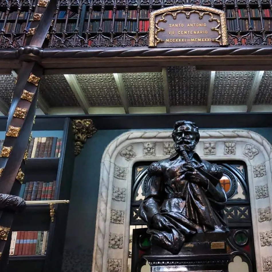 Interior ricamente decorado, biblioteca histórica com prateleiras de livros e escultura de bronze.
