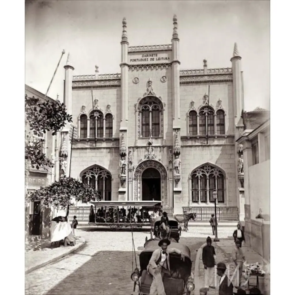 Edifício neogótico com pessoas e carruagens.