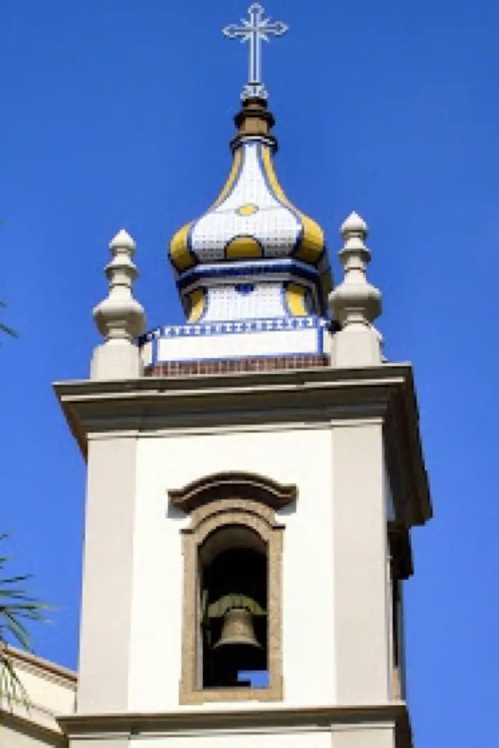 Torre de igreja com sino e azulejos coloridos.