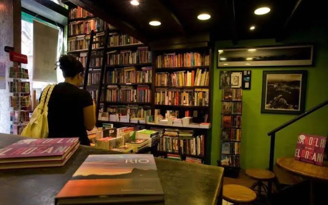 Livro aberto em mesa, livraria ao fundo.