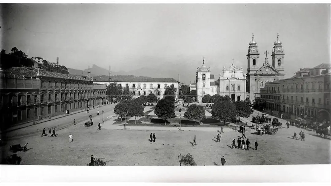 Convento histórico em praça com árvores e pessoas caminhando.