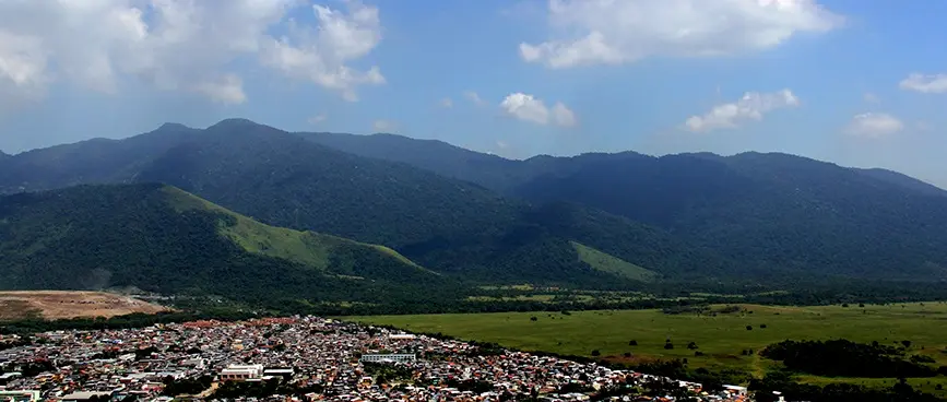 Paisagem montanhosa com morros verdes e cidade colorida.