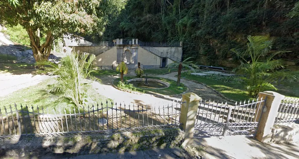 Estrutura histórica cercada por vegetação, com fonte circular e construção de pedra.