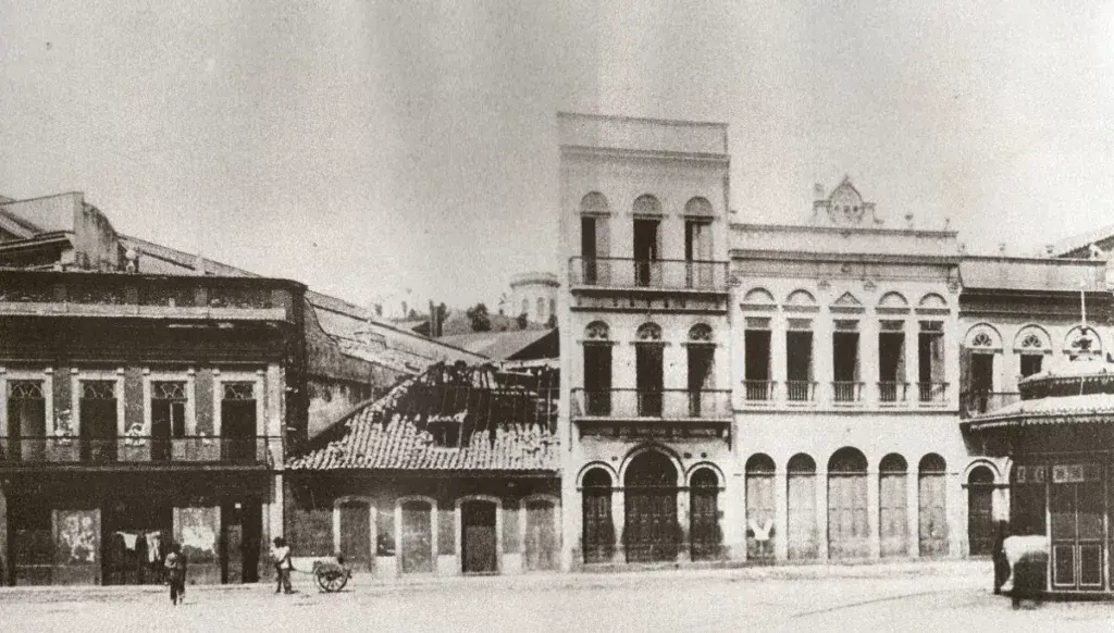 Praça histórica com edifícios antigos e torre ao fundo.