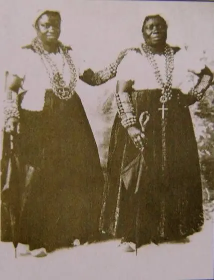 Duas mulheres em preto e branco posam juntos, um vestido preto detalhado e outro com decote aberto.