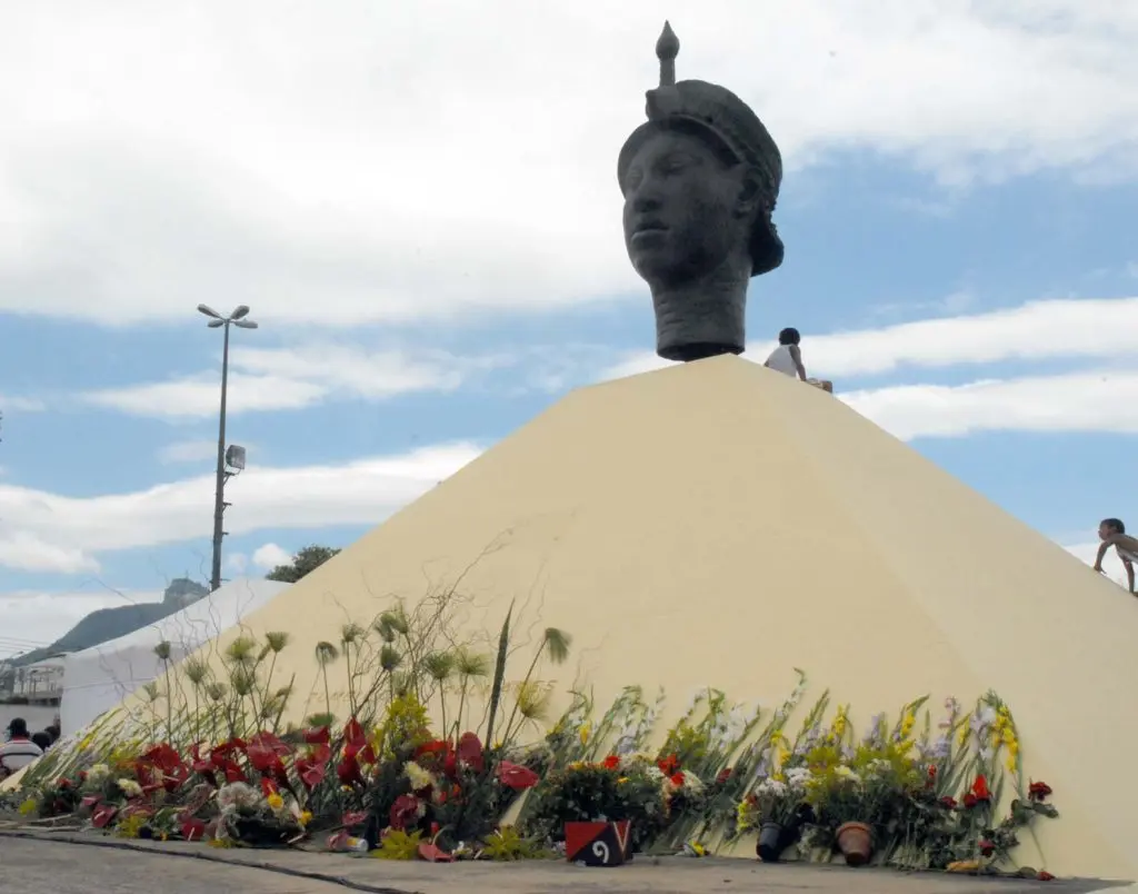 Monumento piramidal com estátua humana e flores coloridas.