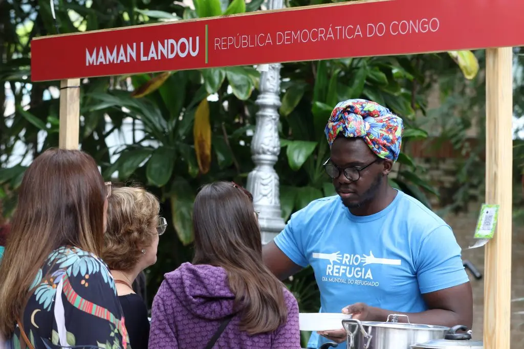 Mulheres olham para homem com turbante em evento com estande da RIO REFUGIA.