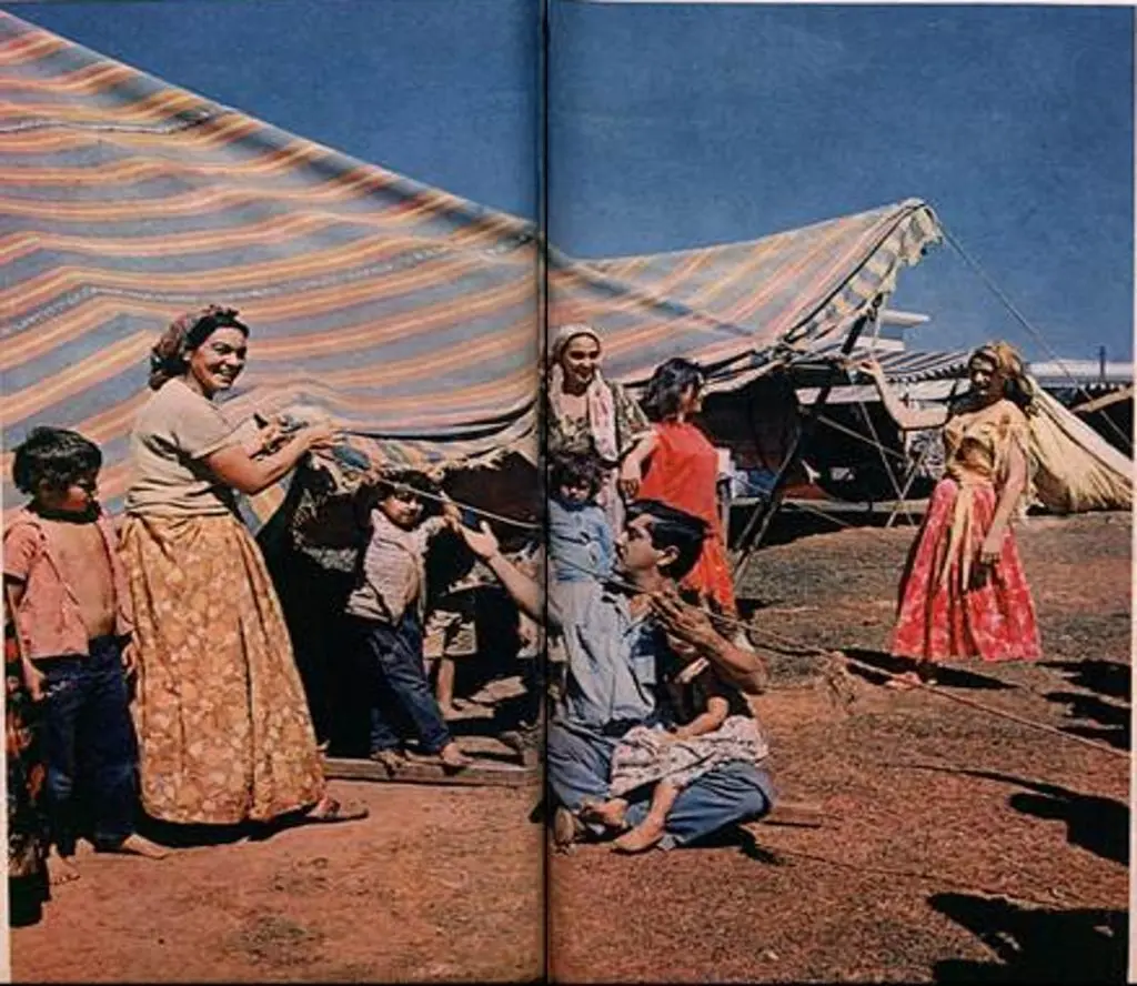 Família cigana em acampamento, roupas tradicionais, dia ensolarado.
