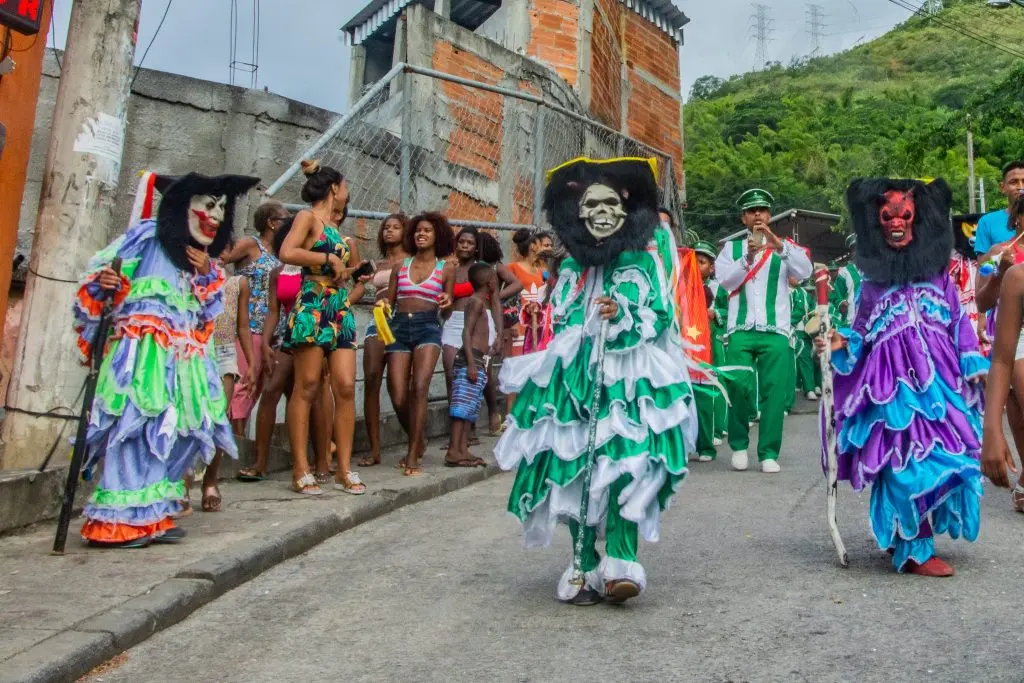 Festa comunitária com pessoas em trajes coloridos e uniformes verdes.