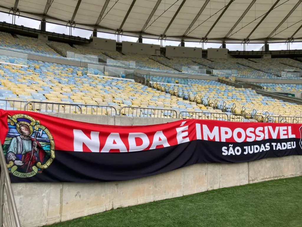 Estádio vazio com banner de São Judas Tadeu e mensagem motivacional.