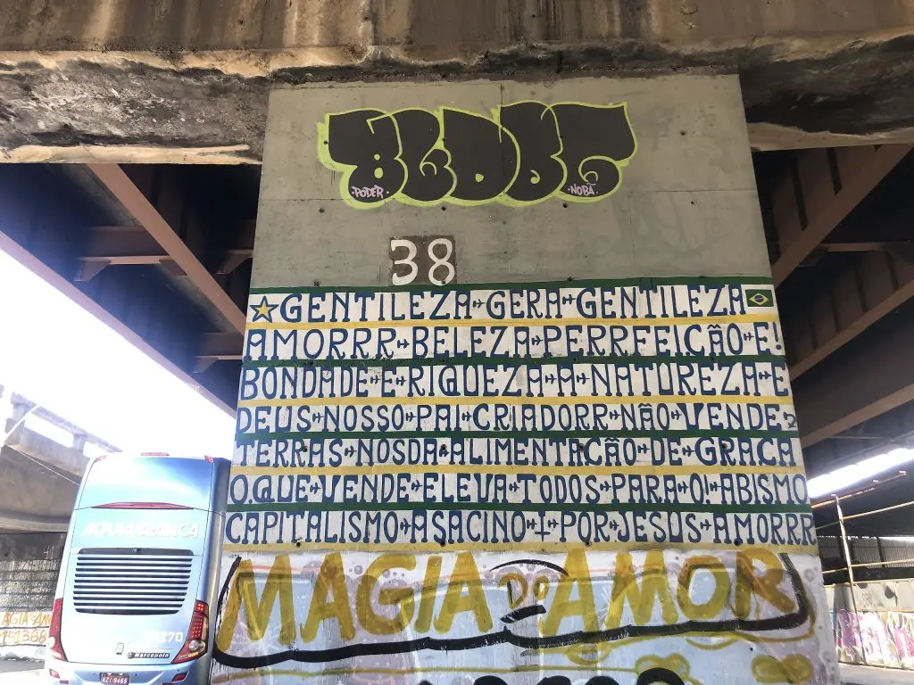 Pilar de concreto com grafite e ônibus ao fundo.