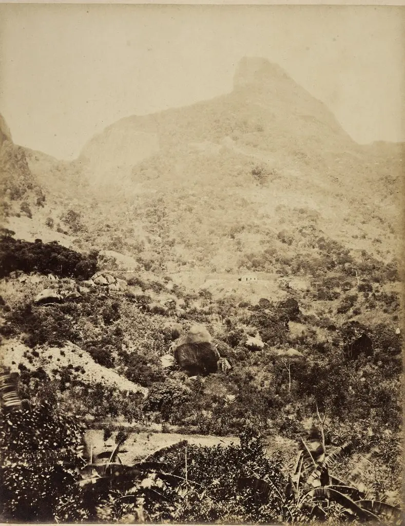 Paisagem montanhosa em preto e branco com formação rochosa, casas e pico de montanha.