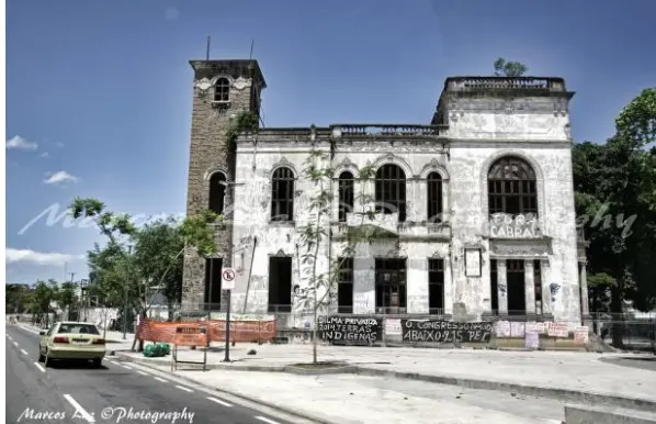 Edifício abandonado em Aldeia Maracanã, com árvores e carro amarelo.