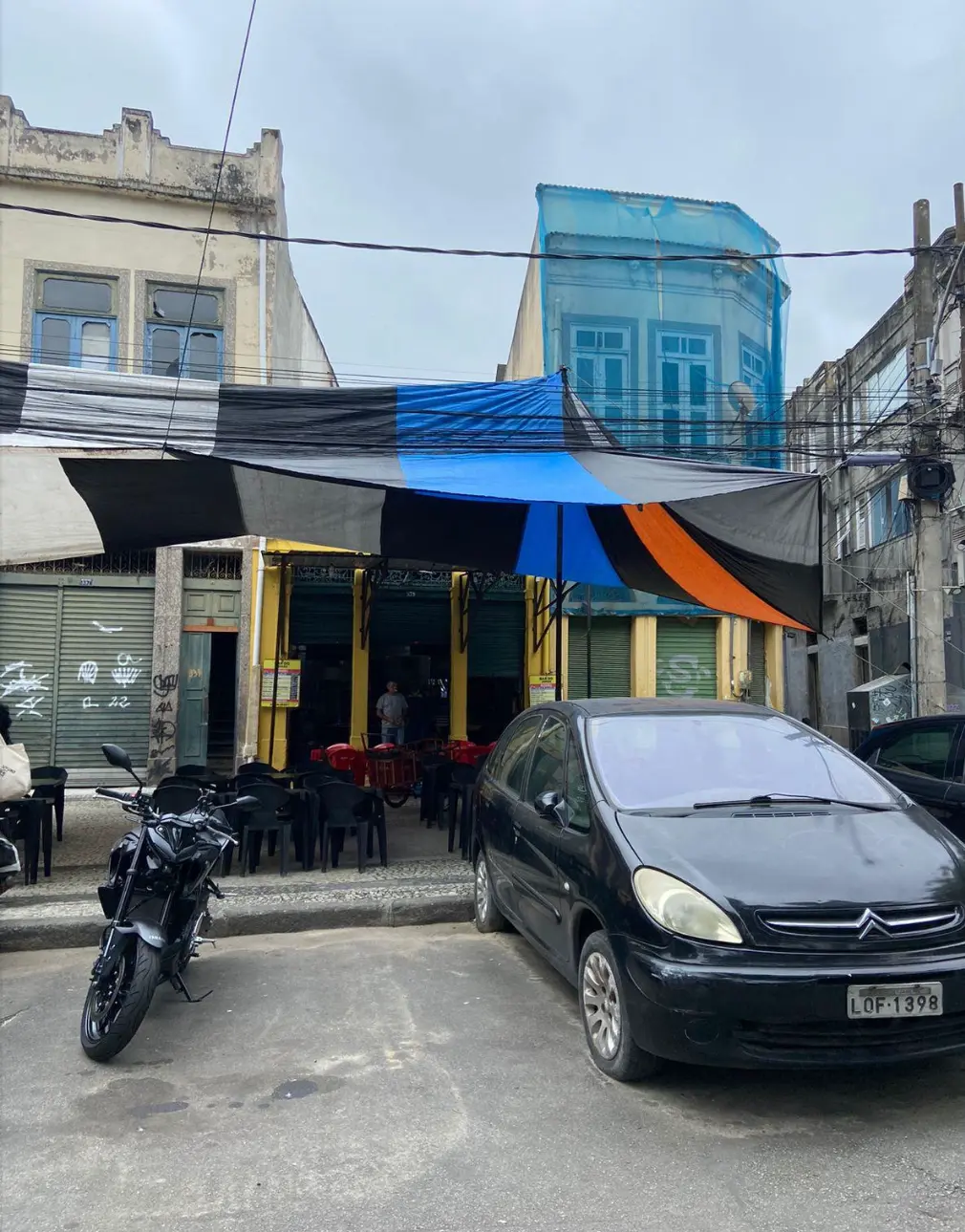 Estabelecimento comercial urbano com motocicleta e carro estacionados.