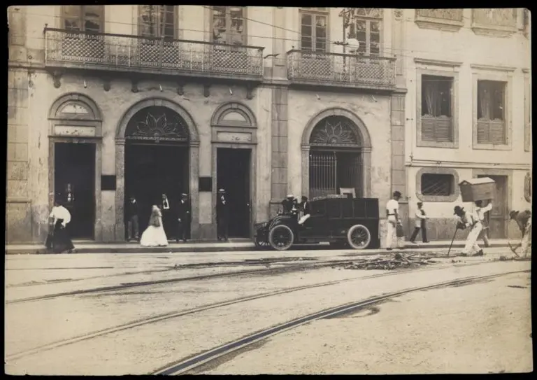 Edifício clássico com pessoas e bondes na frente.