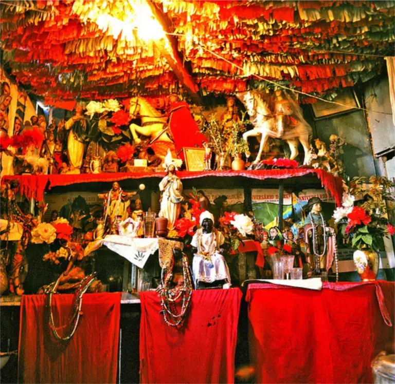Altar de umbanda, em vermelho, com diversas imagens de santos e orixás